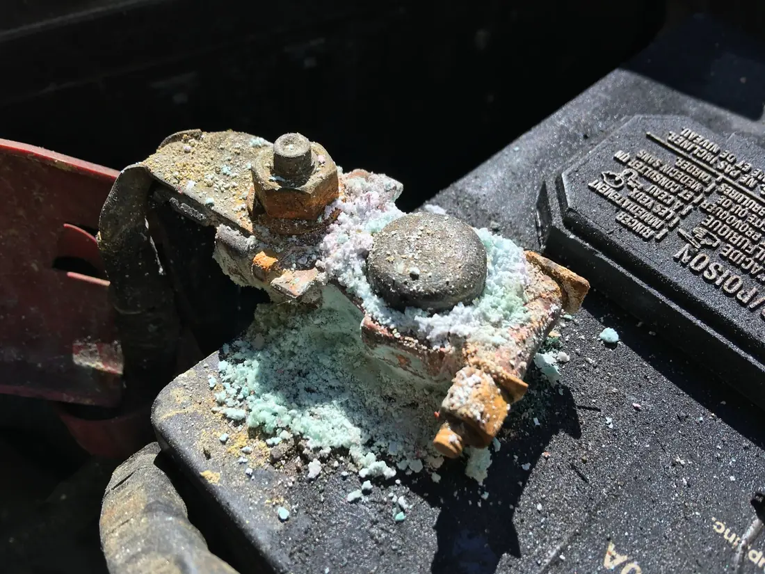Battery post and cable clamp crusted with white and green corrosion, with a rusted clamp bolt.