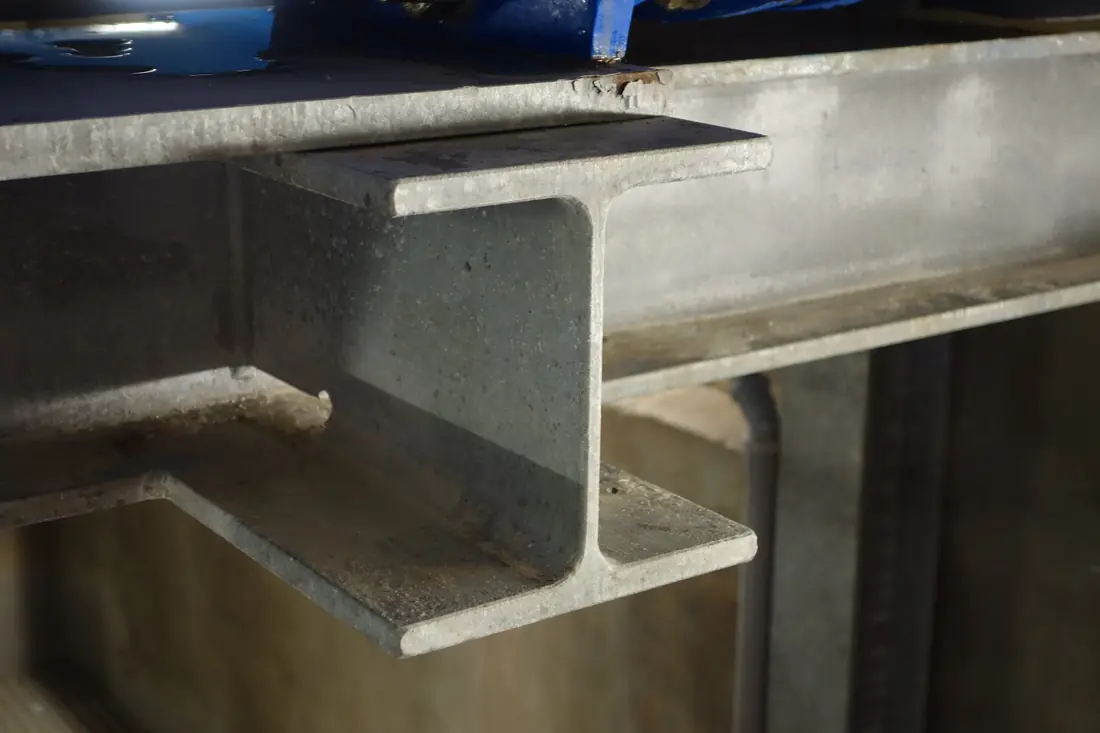 End of a galvanized steel I-beam showing its wide top and bottom flanges joined by a thin vertical web.