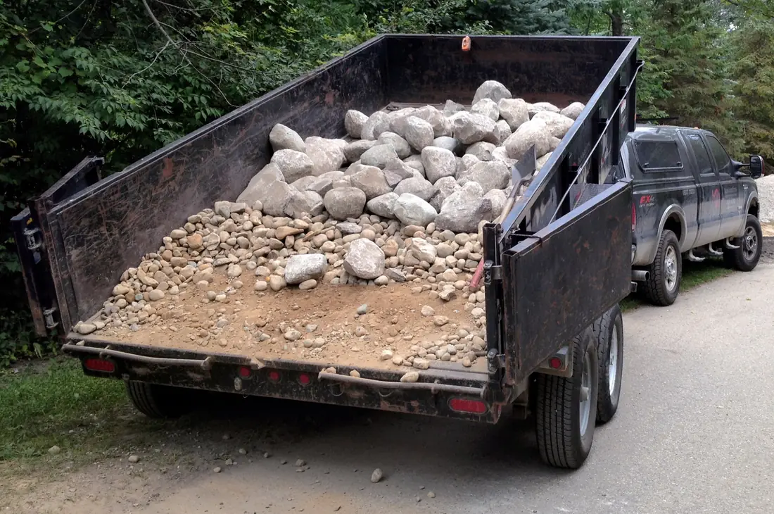 Rear of a dump trailer loaded with rock, both barn-door rear gates swung open.