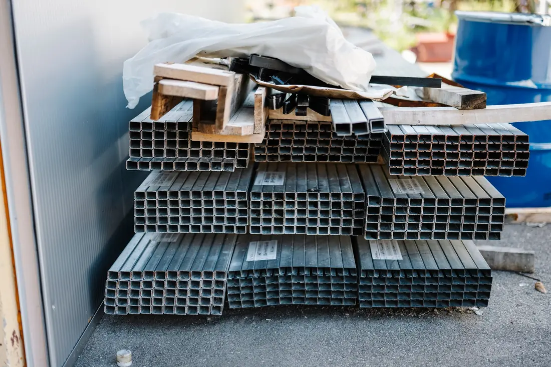 Bundles of square steel tubing stacked against a wall, with their open ends facing the camera.