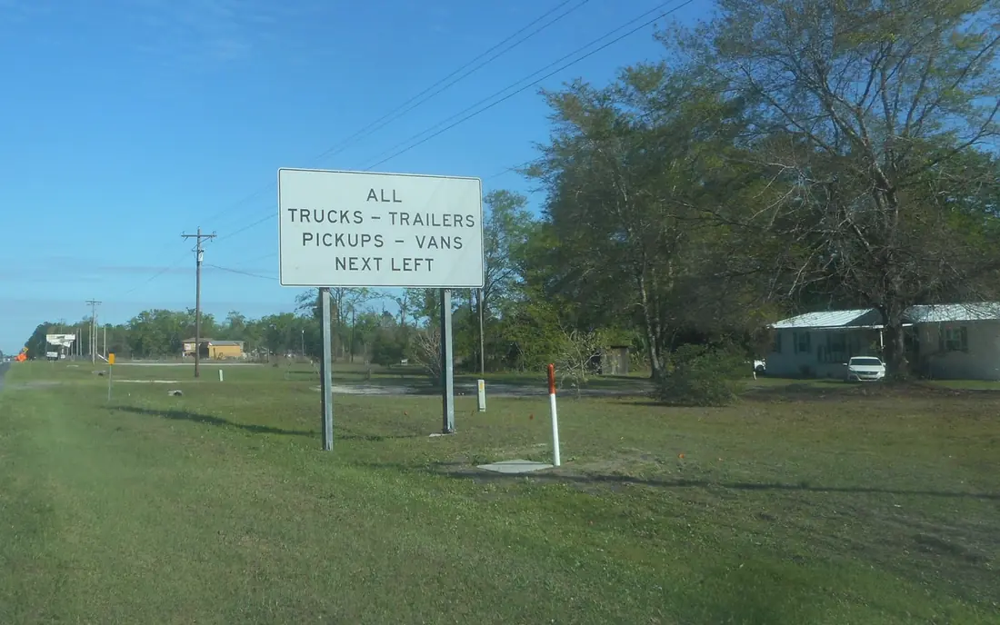 Roadside sign telling all trucks, trailers, pickups, and vans to turn left ahead of a Florida weigh and inspection station.